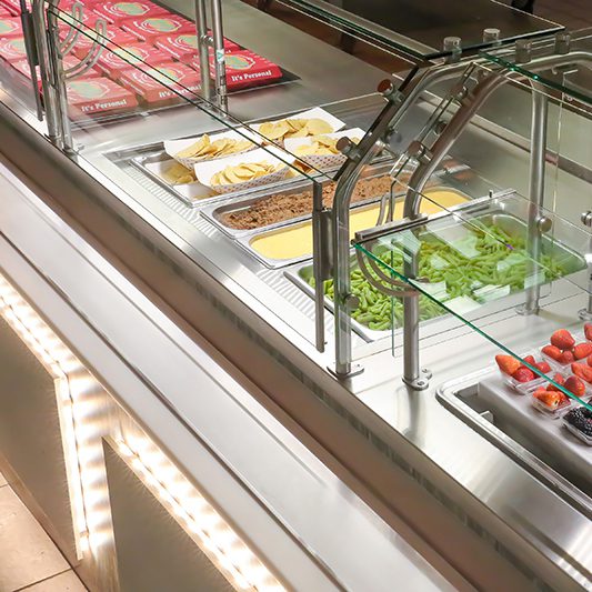 Serving line with glass food guards, taco bar toppings and fresh fruit displays